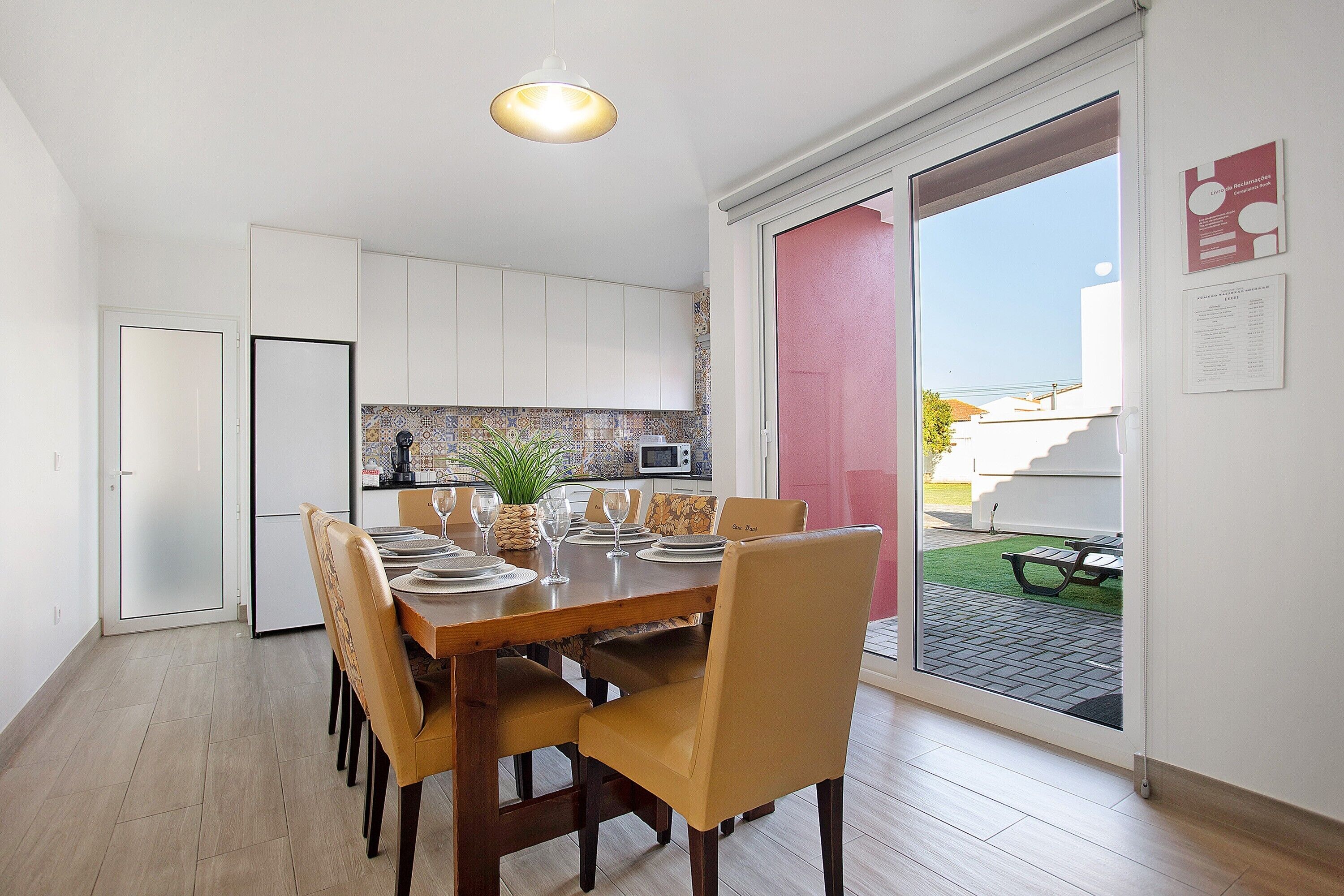 A dining area with a table set for four, a kitchen in the background, and a sliding glass door leading to an outdoor patio.