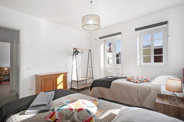 A bedroom with two beds, a wooden wardrobe, a hanging rack, a window with a view, and a ceiling light.