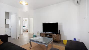 A modern living room with a flat-screen TV, a glass-top coffee table, a sofa, and a wooden cabinet.