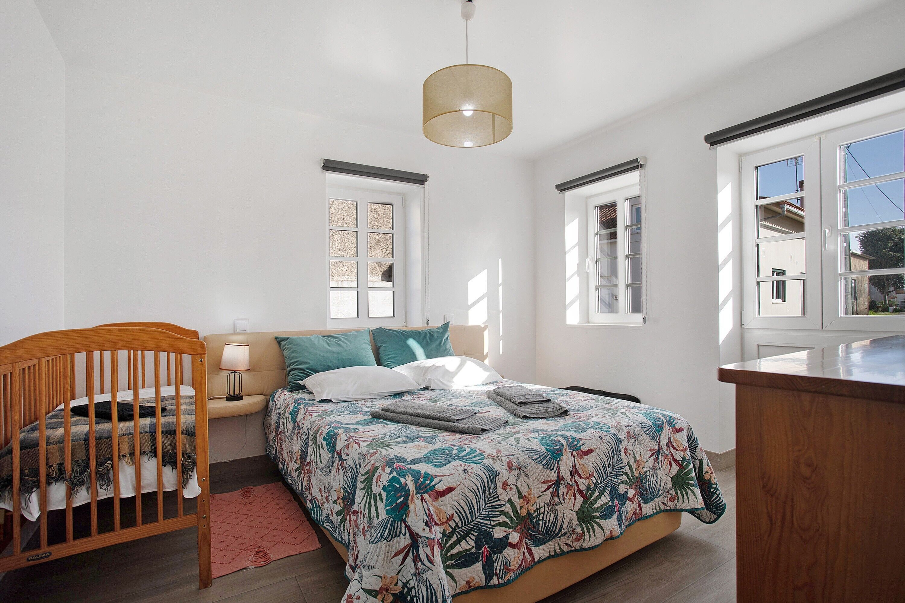 Een slaapkamer met een houten ledikant, een bed met een bloemenbedekking, een bedlampje en een hanglamp.