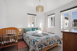 A bedroom with a wooden crib, a bed with a floral bedspread, a bedside lamp, and a pendant light.