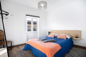 Een slaapkamer met een bed, nachtkastje, lamp, stoel en raam.