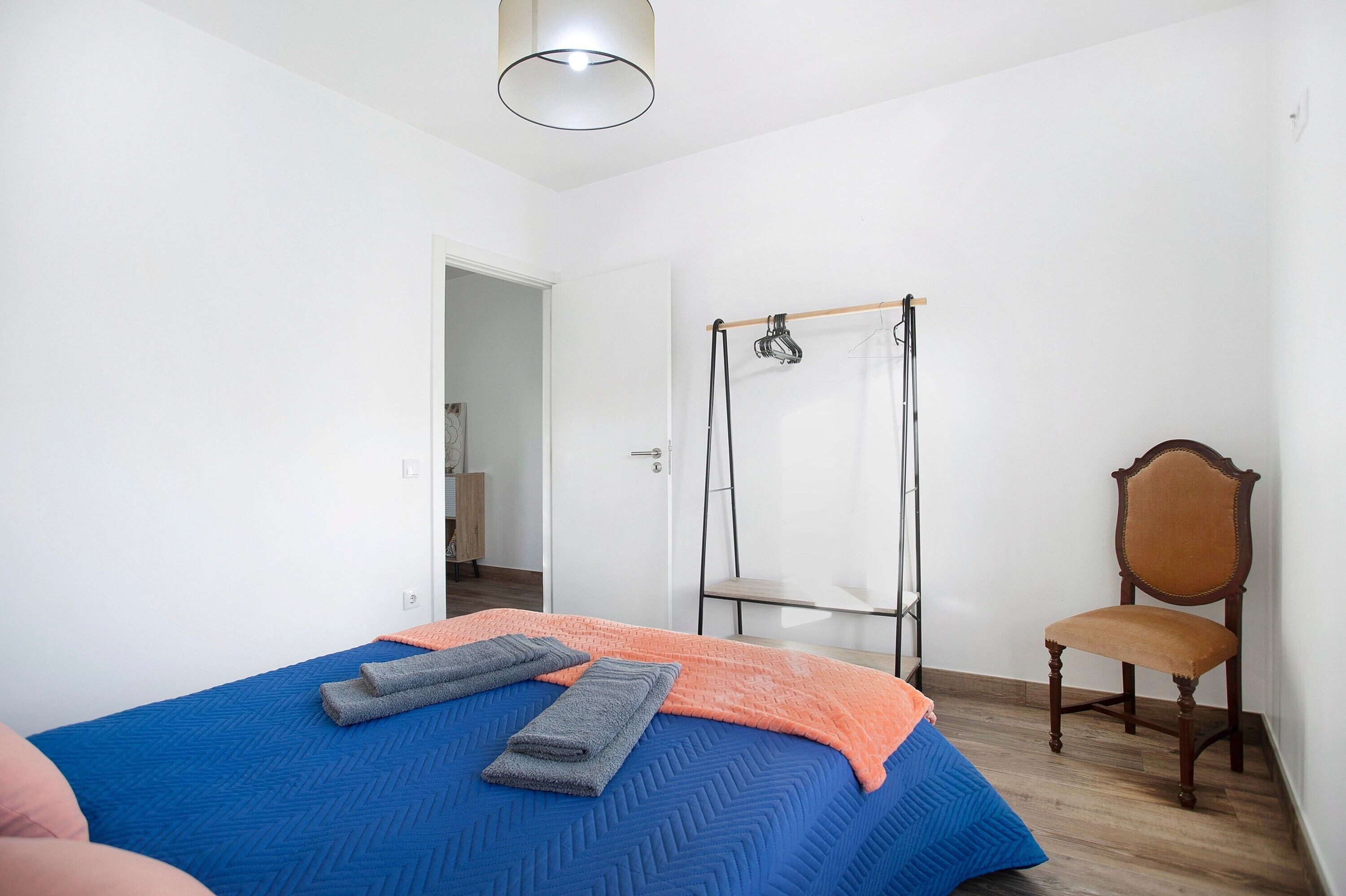 Un dormitorio con cama, una silla, un armario y una percha.