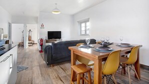 Un coin repas avec une table en bois, des chaises jaunes et un canapé en arrière-plan.