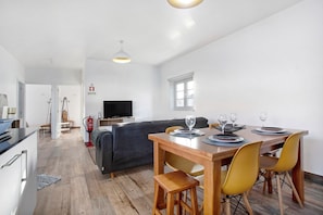 Un coin repas avec une table en bois, des chaises jaunes et un canapé en arrière-plan.