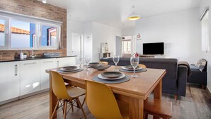 Une cuisine moderne avec des meubles blancs, une table à manger en bois mise avec des assiettes et des verres, et un mur en briques.