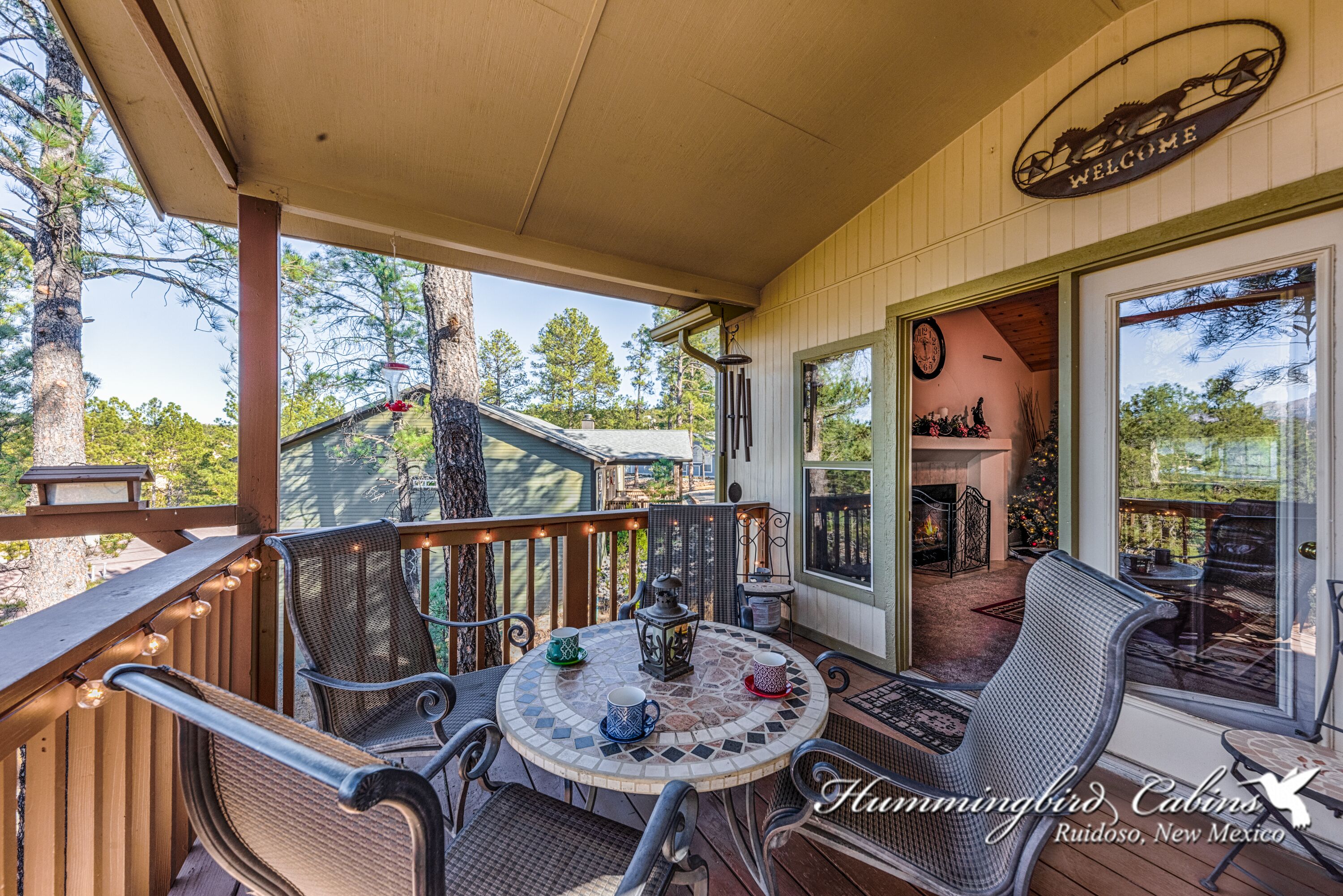 A covered outdoor seating area with wicker chairs and a mosaic table, overlooking a deck and a building with a 'WELCOME' sign.