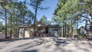 A single-story house with a front porch, surrounded by tall pine trees. - Buendia Cabin | “Good Day” Getaway w/ Hot Tub & Game Room Fun (Ruidoso)