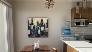 A modern kitchen with a wooden dining table, chairs, and a large painting of wine bottles.