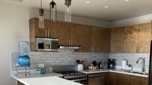 A modern kitchen with wooden cabinets, a central island, stainless steel appliances, and pendant lighting.