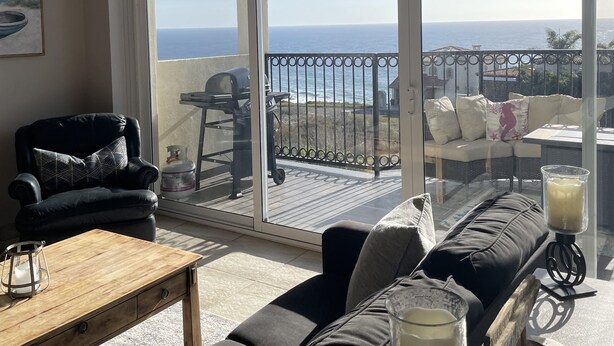 A modern living room with a large sliding glass door leading to a balcony with a view of the sea.
