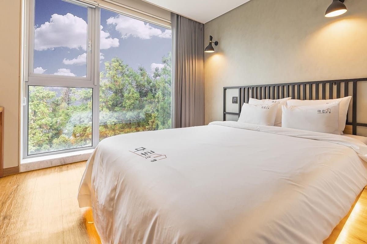 Une chambre d’hôtel dotée d’une grande fenêtre donnant sur les arbres et le ciel.