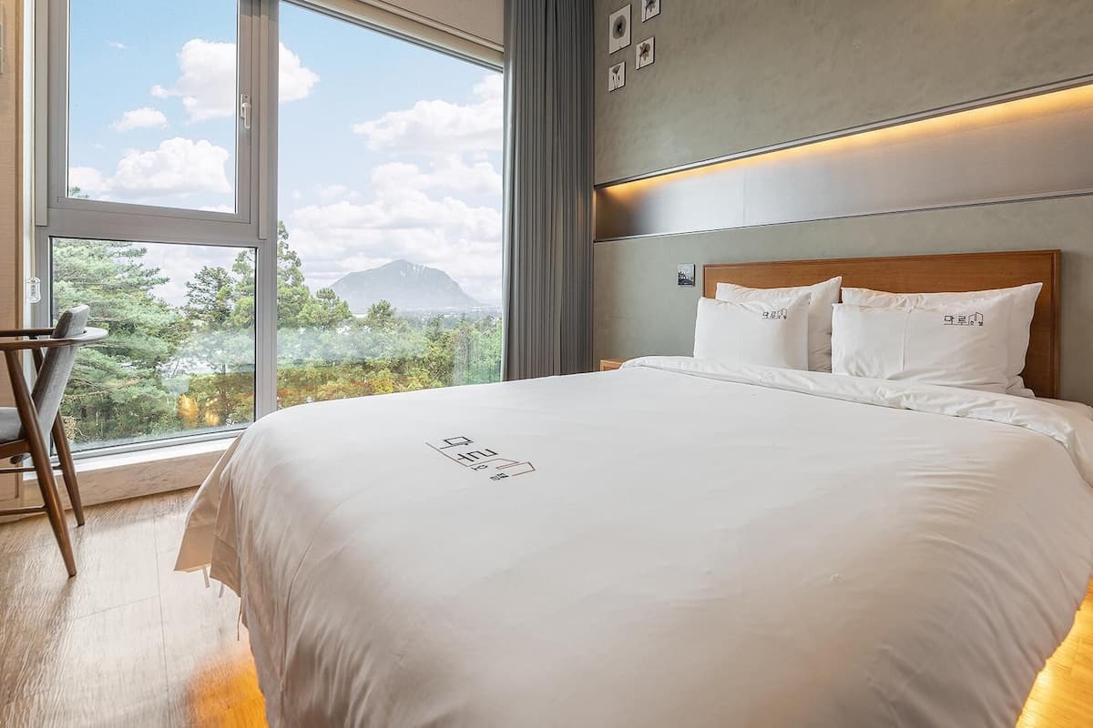 Une chambre d’hôtel avec un grand lit, une vue sur les arbres et les montagnes par la fenêtre, et un plancher en bois.