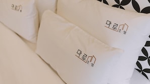 Cama com almofadas brancas, com texto coreano e padrão geométrico em preto e branco.