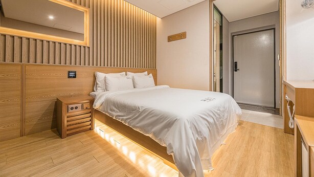 Ein modernes Schlafzimmer mit einem Holz-Kopfteil, einem Nachttisch mit Lampe und einer Tür zu einem Badezimmer.