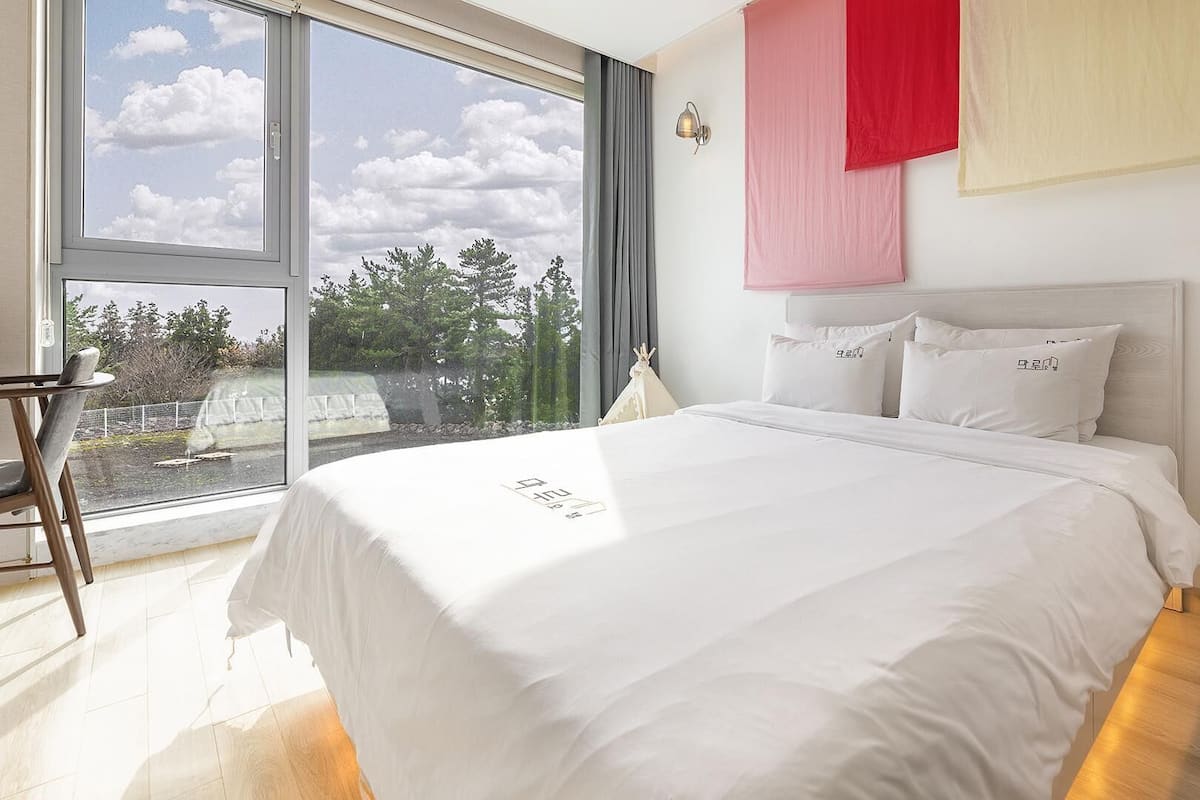 Une chambre moderne avec un grand lit, une vue sur l’extérieur par une fenêtre et une décoration murale aux couleurs rouge et jaune.