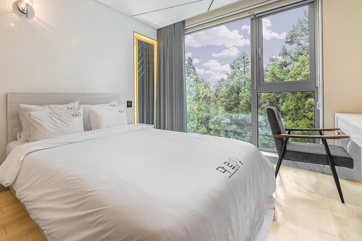 Une chambre moderne avec un grand lit, une chaise et une fenêtre donnant sur la forêt.