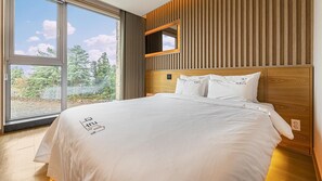 A modern bedroom with a large window, a wooden headboard, and a bed with white linens.