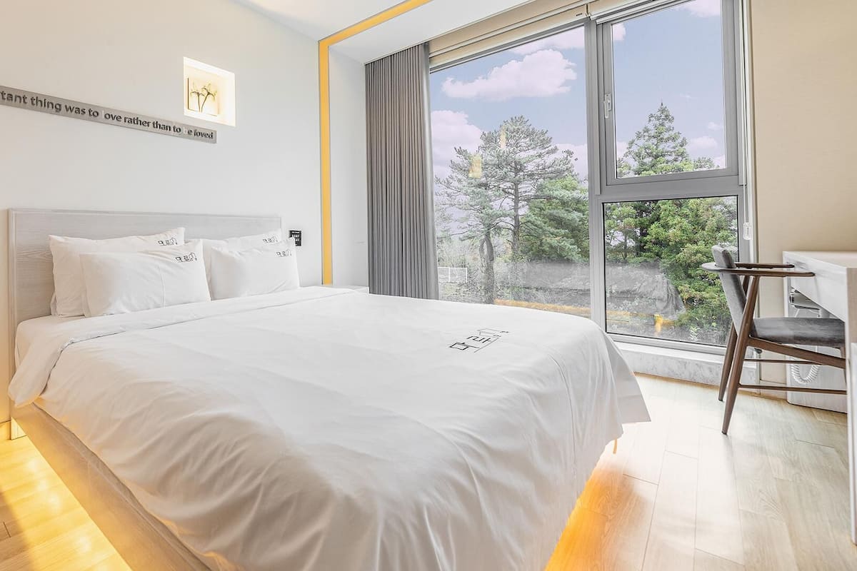 Une chambre moderne avec un grand lit, un bureau et une vue sur les arbres par la fenêtre.