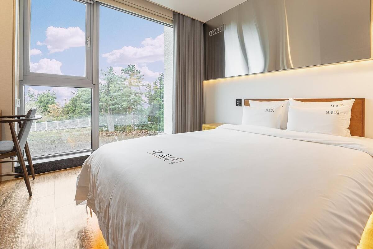 Une chambre d’hôtel avec un grand lit, un bureau et une vue sur les arbres par la fenêtre.