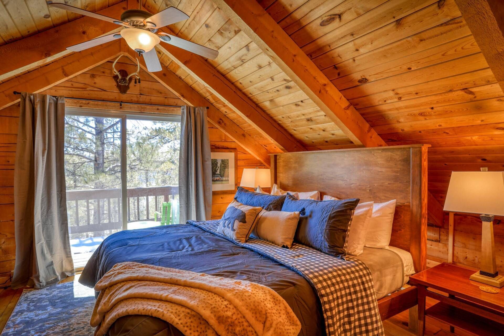 Une chambre confortable, aménagée dans une cabane en bois, avec un grand lit, un ventilateur de plafond et une vue sur l’extérieur.