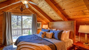 Un dormitorio de cabaña de madera acogedor, con una cama grande, un ventilador de techo y vistas al exterior.