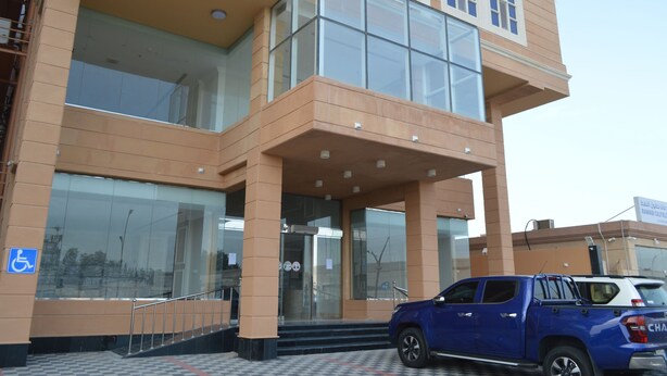 A multi-story building with a glass entrance and a blue pickup truck parked in front. - Karim Hotel (Ras Tanura)