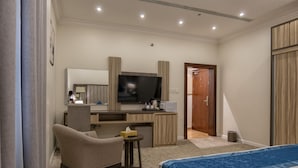 A hotel room with a bed, a desk with a computer, a chair, a TV, and a door. - Karim Hotel (Ras Tanura)