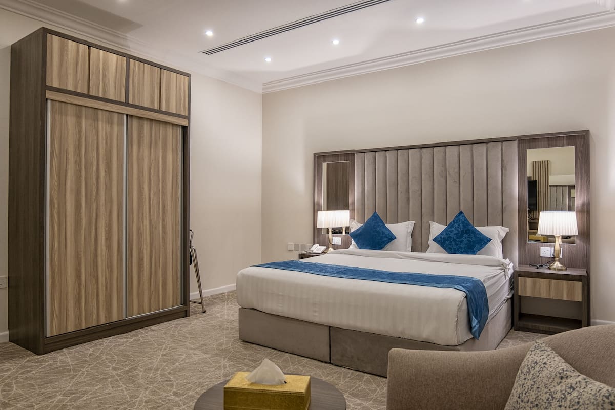 A hotel room with a large bed, a wardrobe, a bedside table with a lamp, and a small round table with a tissue box.