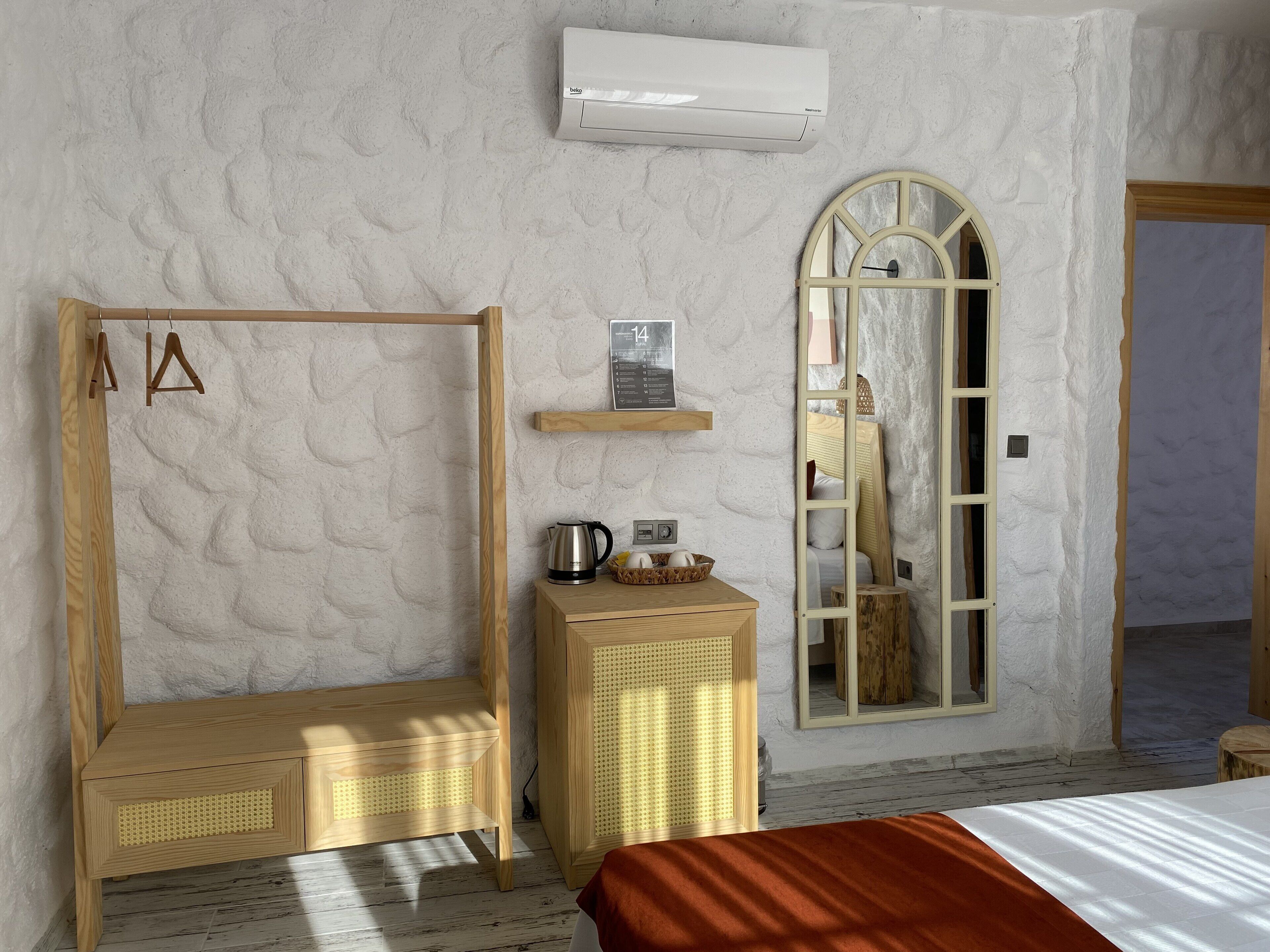 A room with a wooden wardrobe, a small table with a kettle, a mirror, and an air conditioning unit.