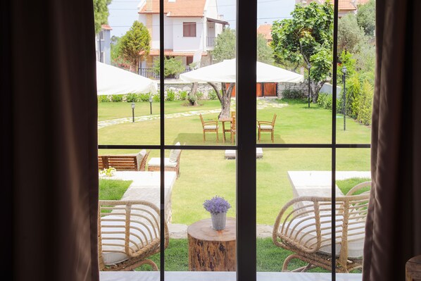 Vista a través de una ventana que muestra una mesa y sillas de madera, un taburete redondo pequeño de madera y una planta en maceta.