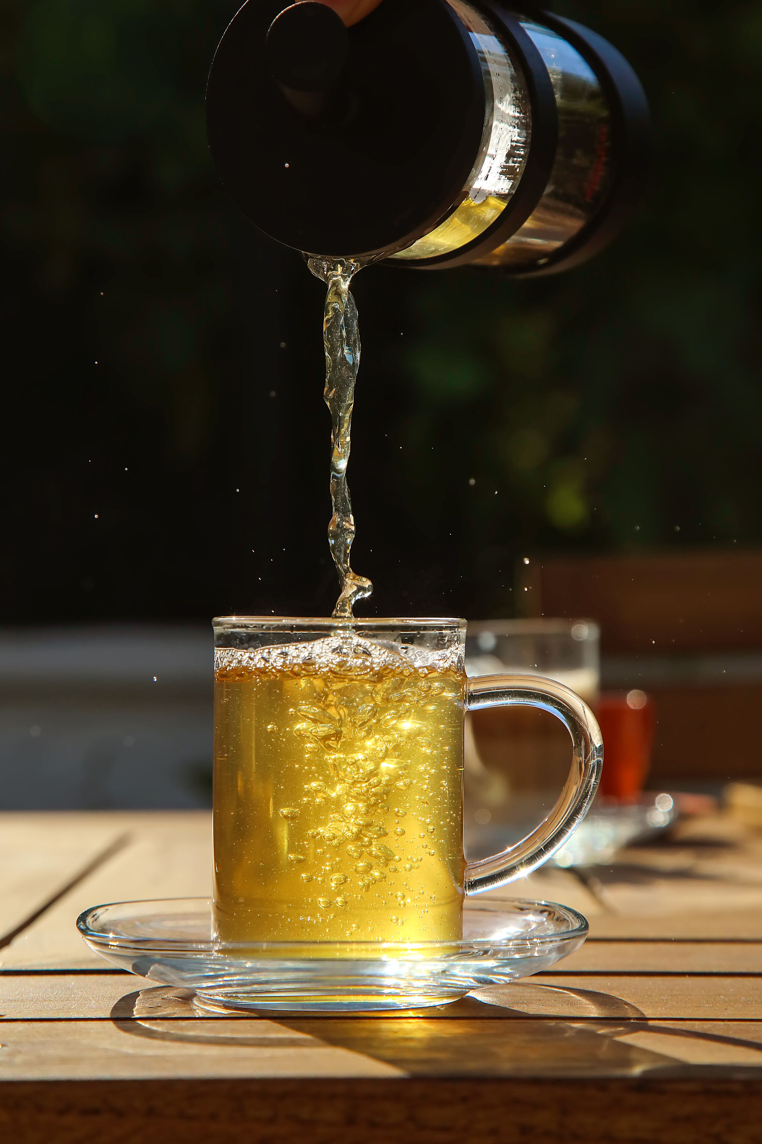 Una taza de vidrio transparente sobre un platito, con una bebida que se está sirviendo.