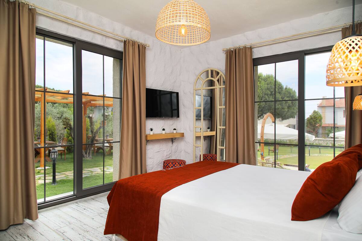 A bedroom with a large bed, a TV, and a view of the garden through large windows.