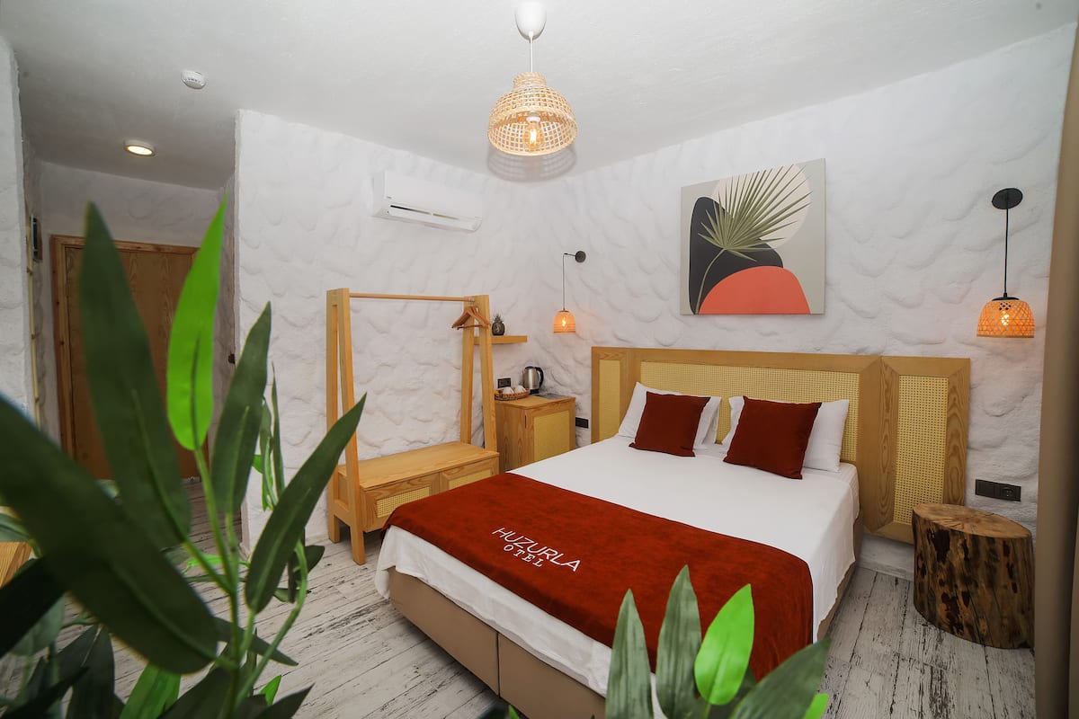 A modern hotel room with a large bed, wooden headboard, a mirror, bedside tables, and a small wooden stool.