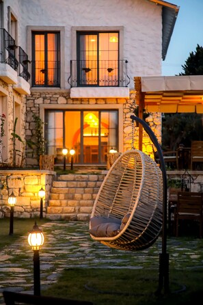 A stone building with a hanging chair in the courtyard, a staircase, and outdoor seating. - Huzurla Otel (Urla)