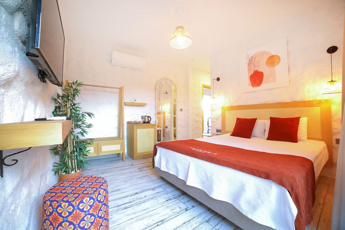 A bedroom with a bed, bedside tables, a mirror, a potted plant, and a wall-mounted TV.