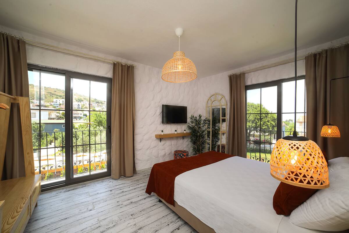 A bedroom with a large bed, a TV mounted on the wall, and a view of a cityscape through large windows.