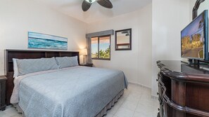 Une chambre d’hôtel avec un lit, un ventilateur de plafond, une télévision et un tableau au mur.