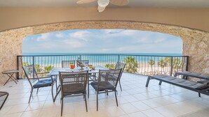 Een balkon met uitzicht op het strand, een tafel met stoelen en een decoratieve schaal.