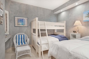 Une chambre avec des lits superposés, une chaise, une table de chevet avec une lampe et un tableau encadré au mur.
