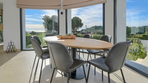 A modern dining area with a round table and six chairs, large windows with a view of greenery, and a ceiling with a light fixture. - Modern and nice villa  with private pool in Benissa, Costa Blanca, Spain for 6 persons (Benissa)