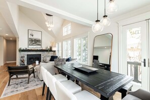 Un espace de restauration moderne avec une longue table, des chaises blanches, une cheminée et de grandes fenêtres.
