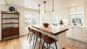 Cozinha moderna com ilha de madeira, banquetas, luminárias pendentes e uma estante.
