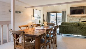 A dining area with a wooden table and chairs, a green sofa, and a stone fireplace. - Snowcreek 1571 (Sun Valley)