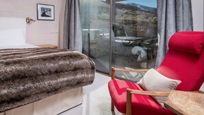 A hotel room with a bed, a red armchair, a glass door leading to a balcony with a table and chairs, and a framed picture on the wall. - Snowcreek 1571 (Sun Valley)