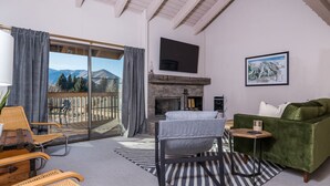 A living room with a fireplace, a green sofa, and a view of mountains through large sliding doors. - Snowcreek 1571 (Sun Valley)