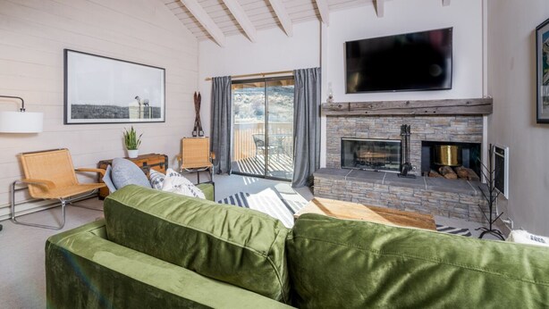 A living room with a green sofa, a fireplace, a television, and a large window with curtains. - Snowcreek 1571 (Sun Valley)