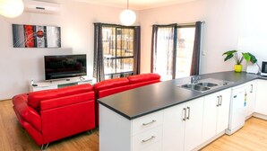 A modern kitchen with a central island, white cabinets, and a red sofa. - Unique Cottages Gawler (Gawler South)