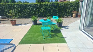 A patio with artificial grass, a round table, and blue chairs. - House in the countryside, very quiet area. (Damparis)