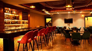 Zona de bar con una barra larga, taburetes rojos y una pared de ladrillo con un televisor montado arriba.